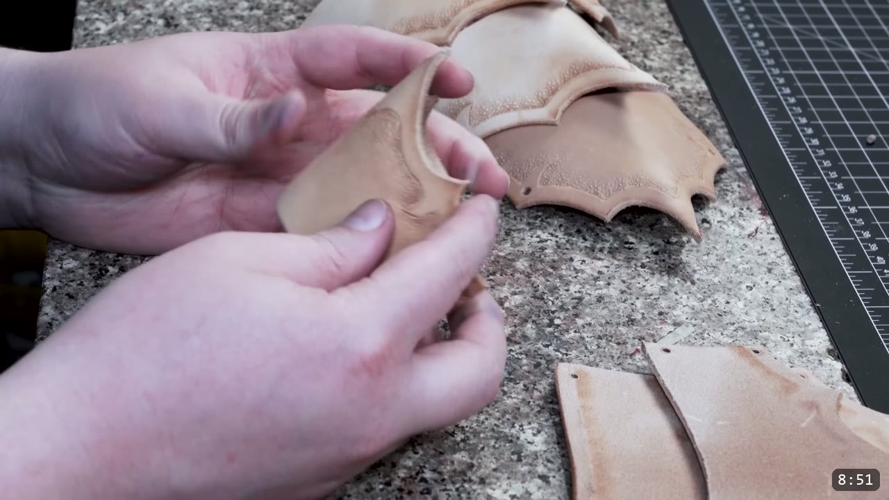 Fantasy Spaulders Build Guide: Leather Shoulder Armor from a Flat Pattern 8 hands pinch-molding a damp tan plate into a shallow curve, with tooled plates resting on a granite slab