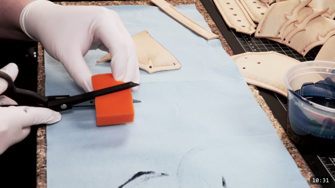 Fantasy Spaulders Build Guide: Leather Shoulder Armor from a Flat Pattern 9 gloved hands trimming an orange high-density sponge with scissors on blue paper, a cup of blue dye and dyed plates nearby