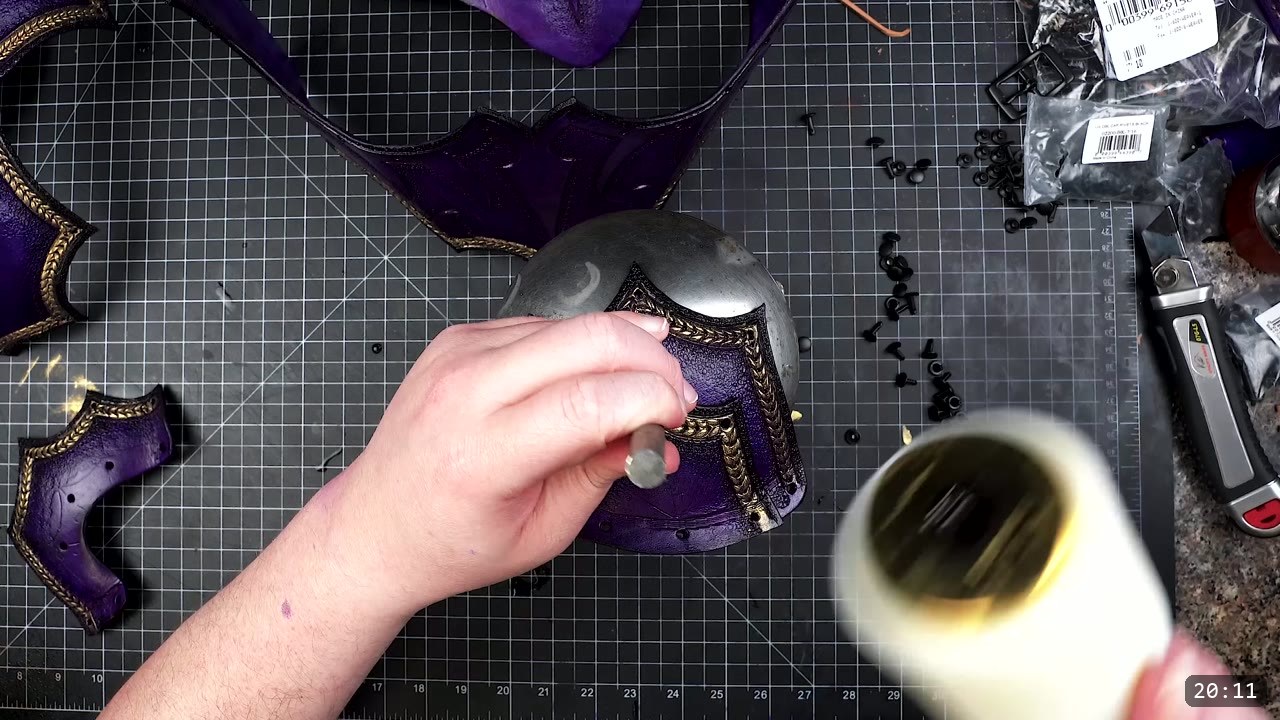 Female Leather Breastplate Build Guide: Articulated Fantasy Armor, Step by Step 13 setting a black double-cap rivet on a purple and gold breastplate piece over a steel doming ball, with bags of black rivets and a rivet setter nearby