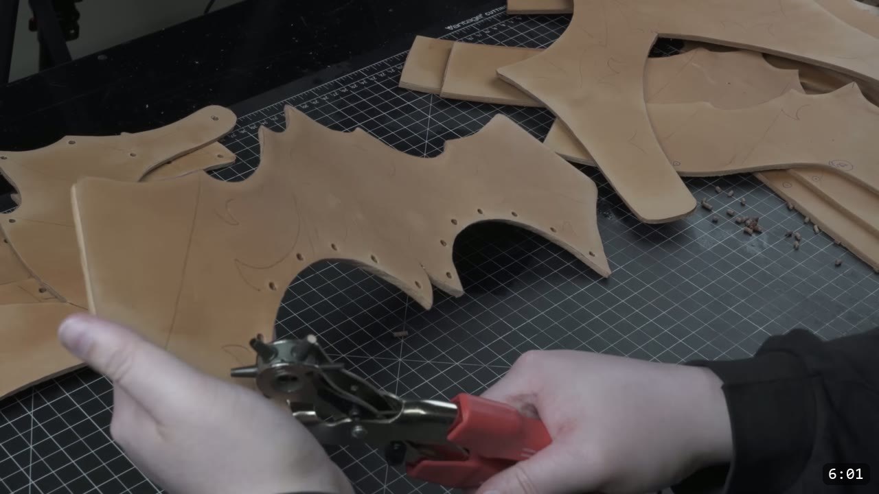 Female Leather Breastplate Build Guide: Articulated Fantasy Armor, Step by Step 5 cut tan leather breastplate pieces with punched rivet holes on a black cutting mat, a red-handled rotary hand punch in hand