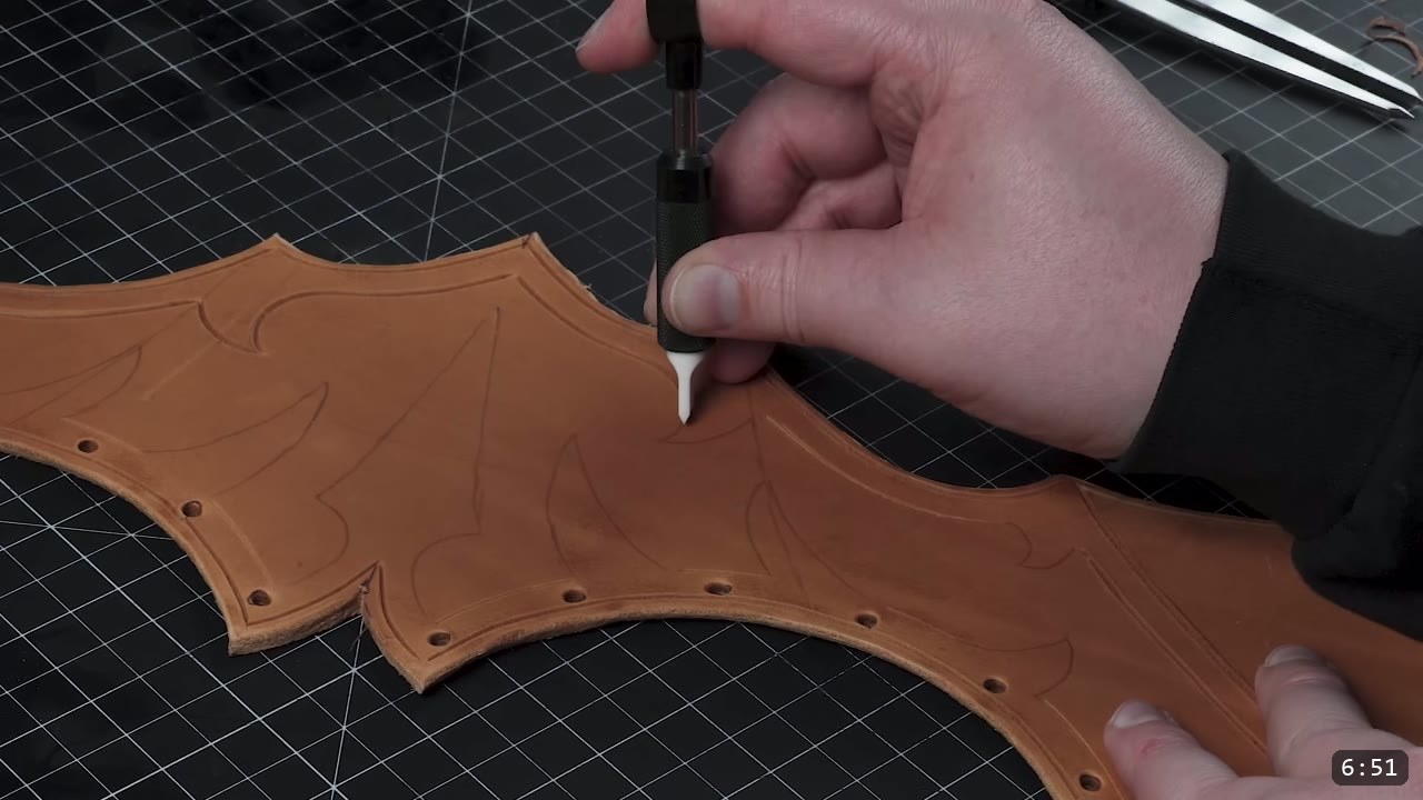 Female Leather Breastplate Build Guide: Articulated Fantasy Armor, Step by Step 6 a cut tan breastplate piece with carved design lines and punched holes on a cutting mat, a hand tool working the surface