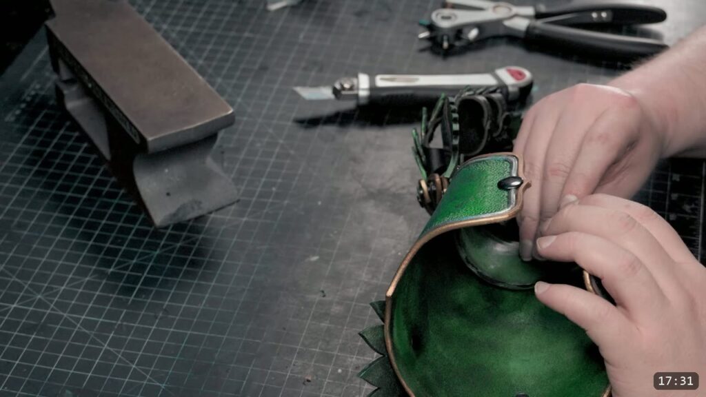 hands fitting the snapped green cuff into its wrist shape over a steel bench stake, a box cutter and hole punch on the mat