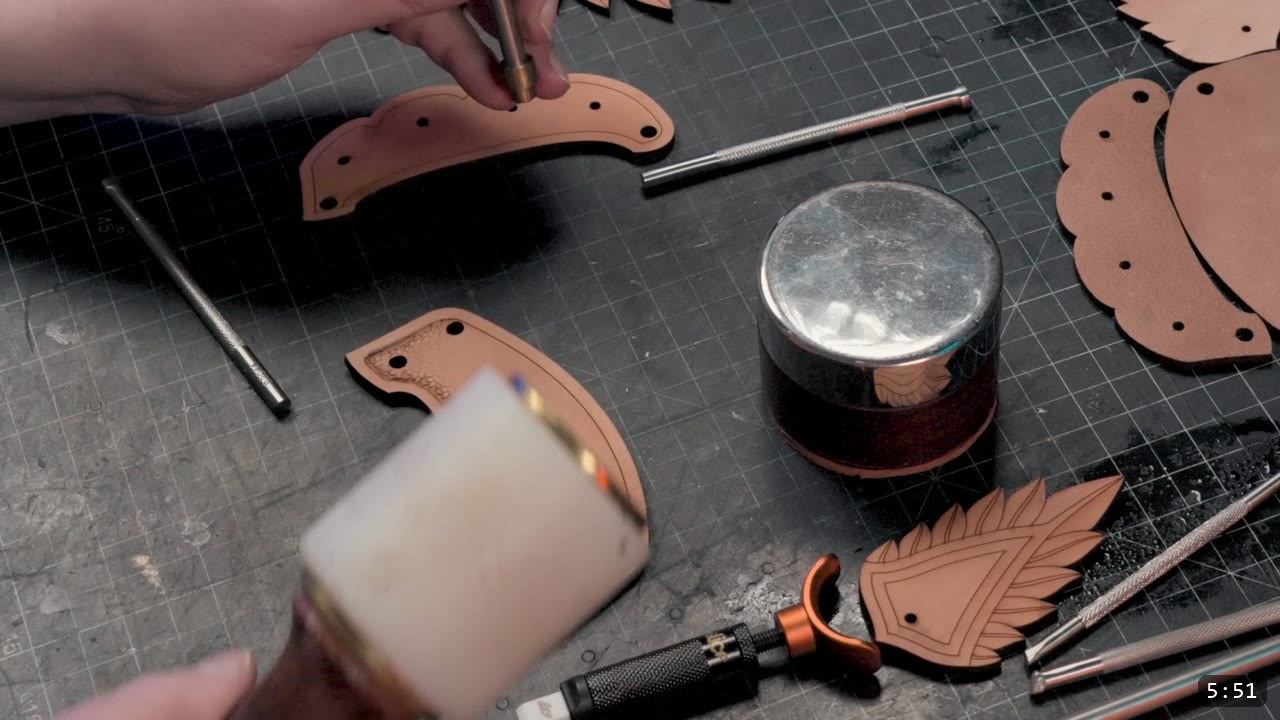 a maul and modeling tool working the edge of a curved cuff piece, a round steel anvil and tooled feather scales on the mat