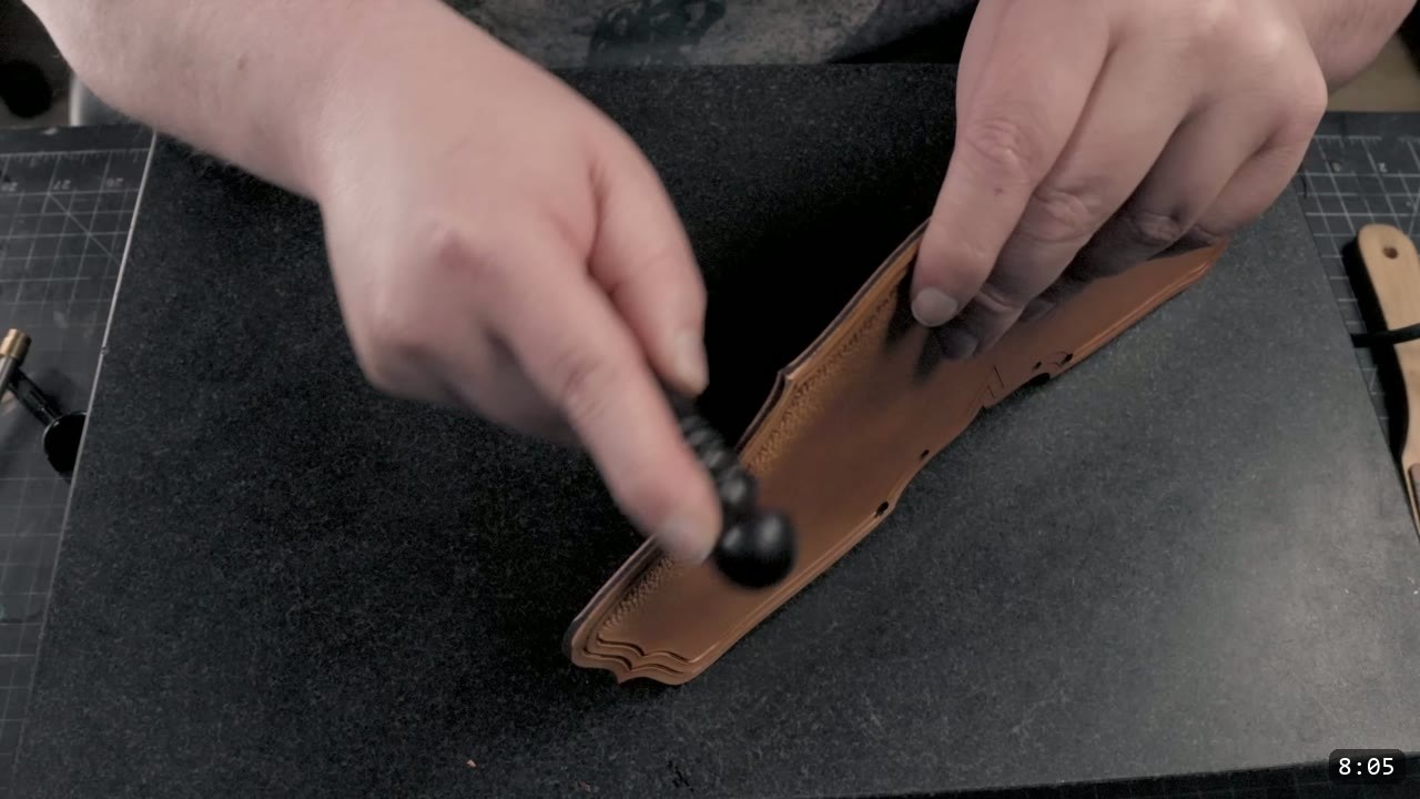 hands dishing a tooled tan cuff piece over a black foam block with a rounded ball-end modeling tool
