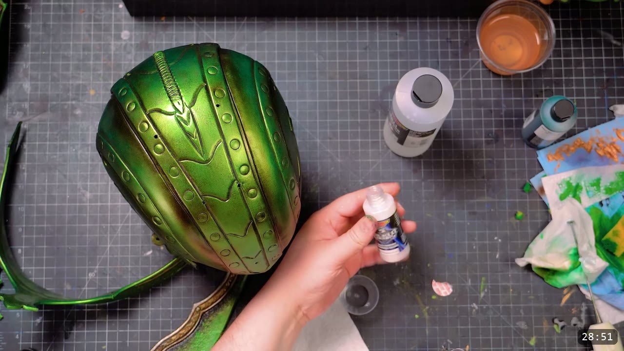Leather Elven Helmet Build Guide: Visor, Comb, Tail, and a Green Metallic Finish 12 the painted metallic-green helmet core with tooled wavy lines and rivet dots, a hand holding a small white paint bottle beside other acrylic bottles