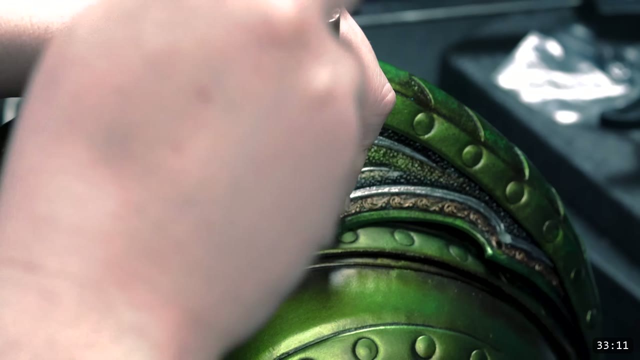Leather Elven Helmet Build Guide: Visor, Comb, Tail, and a Green Metallic Finish 13 macro of the finished helmet trim showing metallic green riveted panels, a silver band, bronze scrollwork, and black antiquing in the recesses