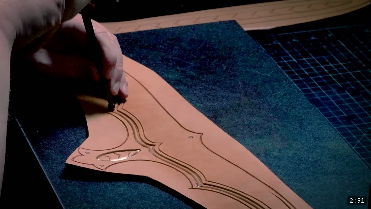 Leather Elven Helmet Build Guide: Visor, Comb, Tail, and a Green Metallic Finish 4 a hand carving border lines and a scroll motif into a damp tan leather piece on a dark work surface