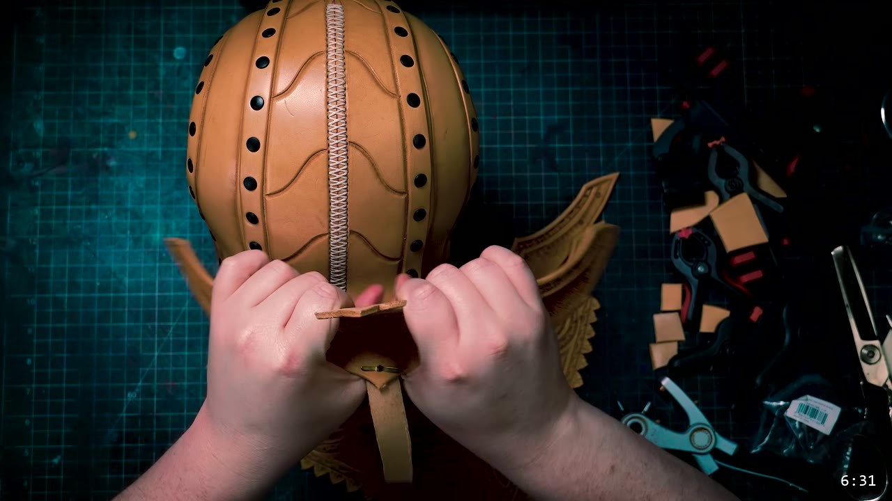 Leather Elven Helmet Build Guide: Visor, Comb, Tail, and a Green Metallic Finish 5 two hands working at the base of the laced helmet core, fitting the tail and marking the retaining-strap holes, with a carved feathered plate behind