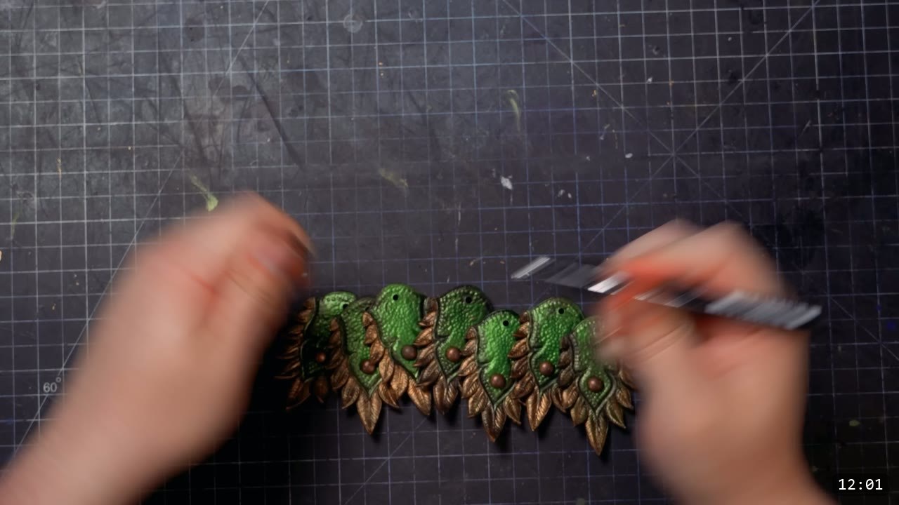 a row of assembled scales with silver-edged bronze tips and a copper stud in each green center, worked flat on the cutting mat