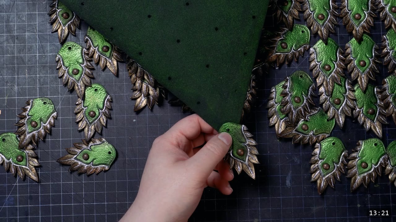 hand placing finished scales in overlapping rows around a dark green back panel dotted with punched rivet holes