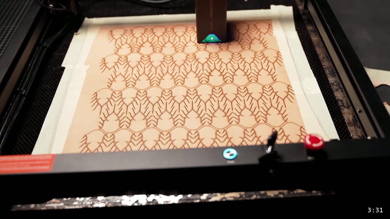 laser cutter working across a large tan leather sheet, cutting a full field of interlocking feather-shaped scale outlines