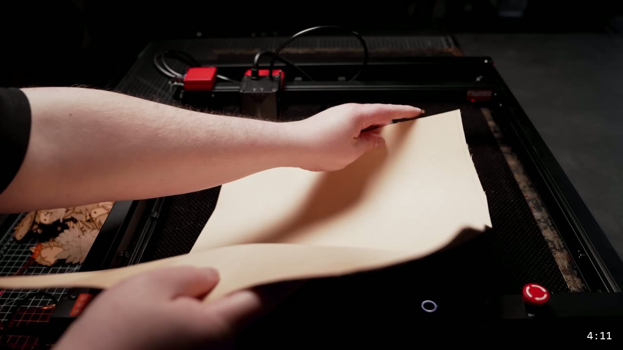 hand laying a large sheet of tan vegetable-tan leather onto the laser bed, a previously cut scale sheet resting at the left