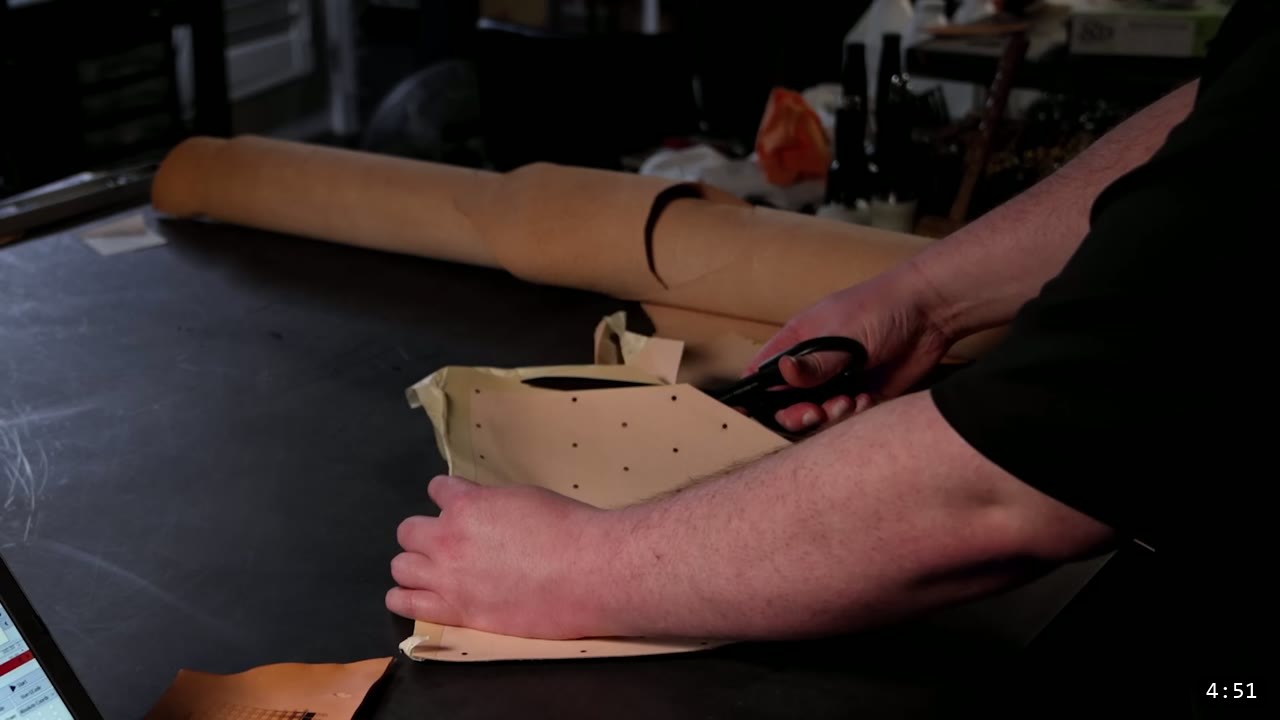 trimming the back panel free from the hide with heavy scissors, rows of pre-punched rivet holes already cut into the tan leather