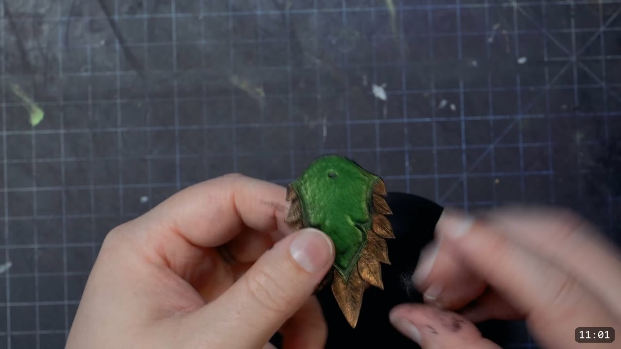 close-up of a single finished scale, green pebbled center and bronze feathered tips, fingers twisting the outer points up and out