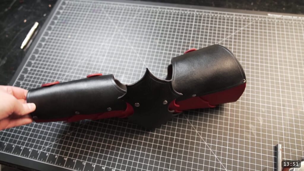 the finished fantasy leather arm armor, black plates with red accents and a barbed elbow, held over the cutting mat