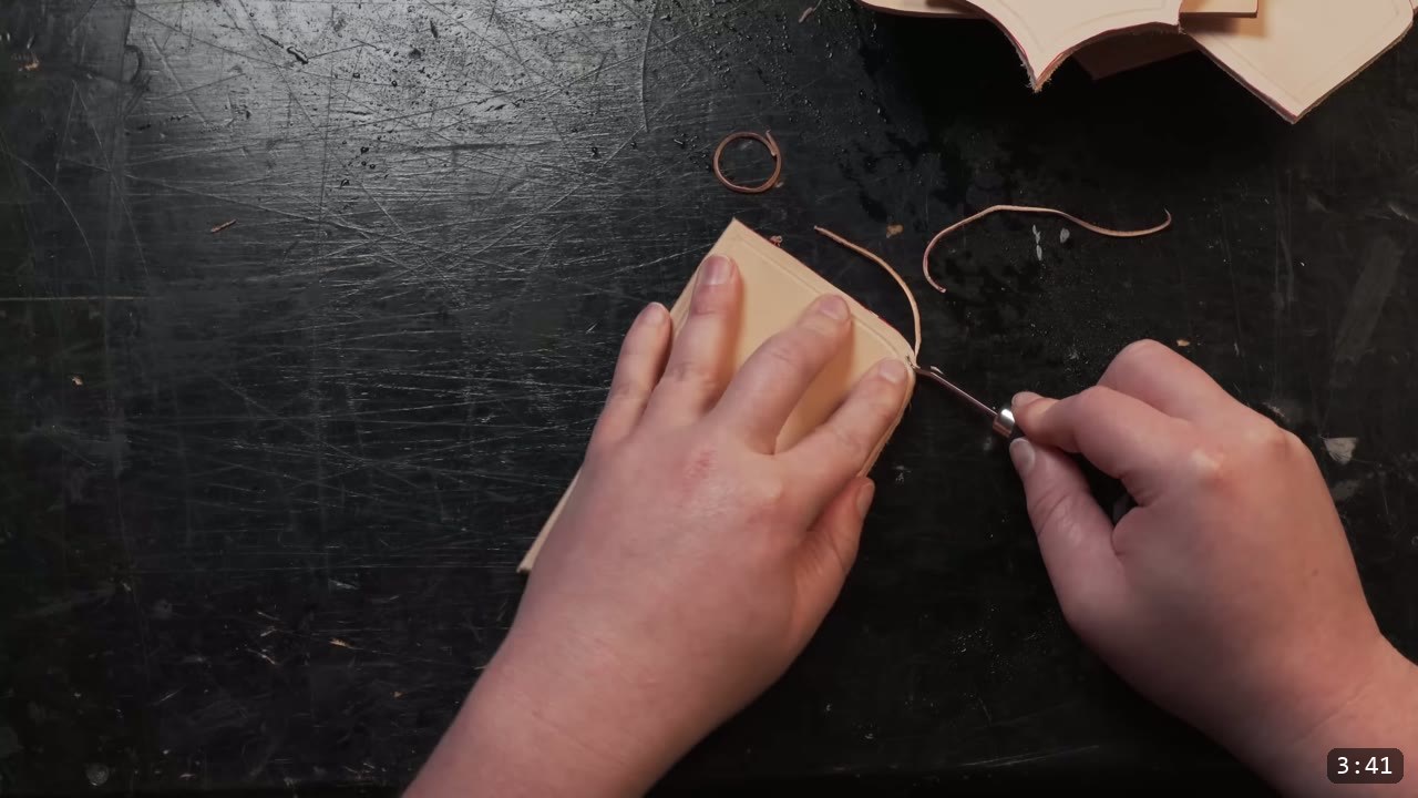 Leather Arm Armor Build Guide: Fantasy Vambrace, Rerebrace, and Elbow 6 running an edge tool along the border of a small tan leather piece, thin leather curls from beveling on the bench