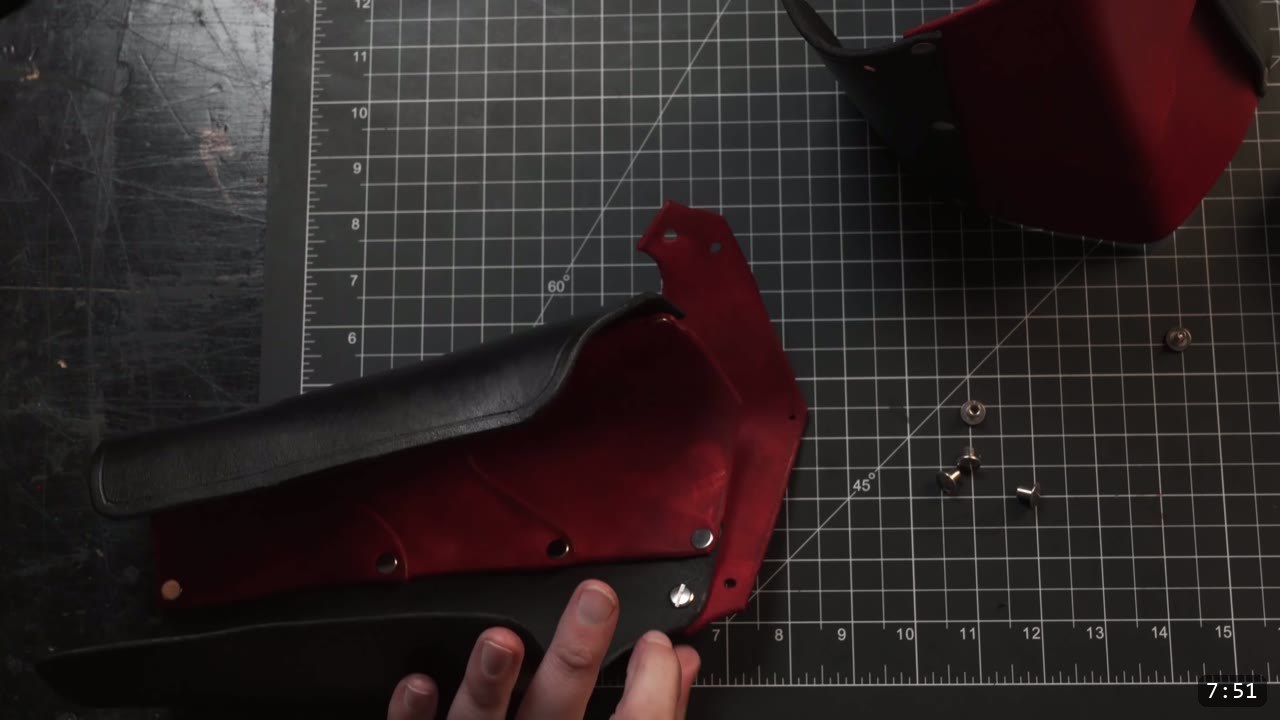 Leather Arm Armor Build Guide: Fantasy Vambrace, Rerebrace, and Elbow 10 aligning a black arm-armor plate against a red vambrace piece on a cutting mat, loose silver rivets and Chicago screw posts ready