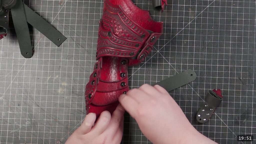hands fitting the last scales onto the assembled red forearm and cuff, with a snap closure strap at the edge of the mat