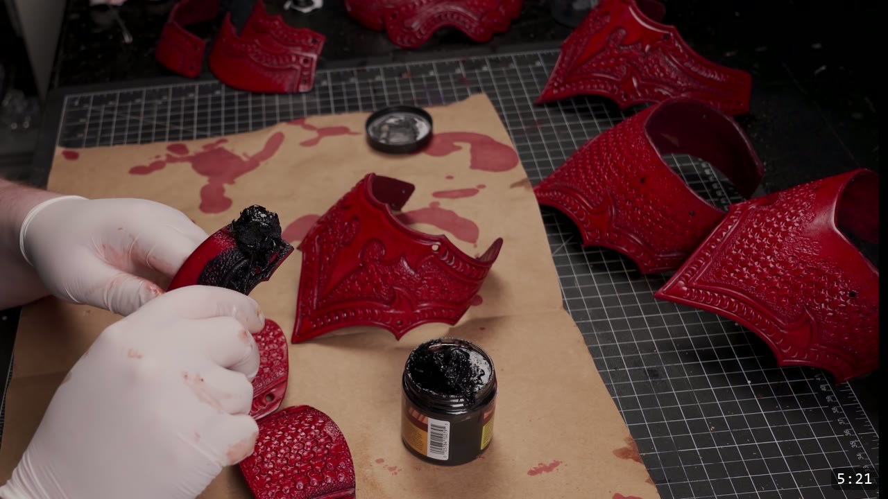 Articulating Leather Gauntlets Build Guide: A Fantasy Set from a Flat Pattern 6 gloved hands rubbing black antique paste into a red tooled leather piece beside a jar of black antique finish