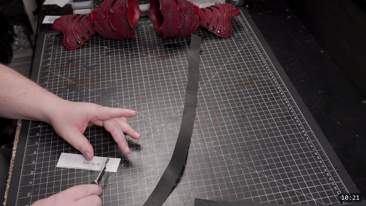 Articulating Leather Gauntlets Build Guide: A Fantasy Set from a Flat Pattern 9 a hand cutting a long thin dark leather strap on a gridded cutting mat with the finished red hand scales resting behind
