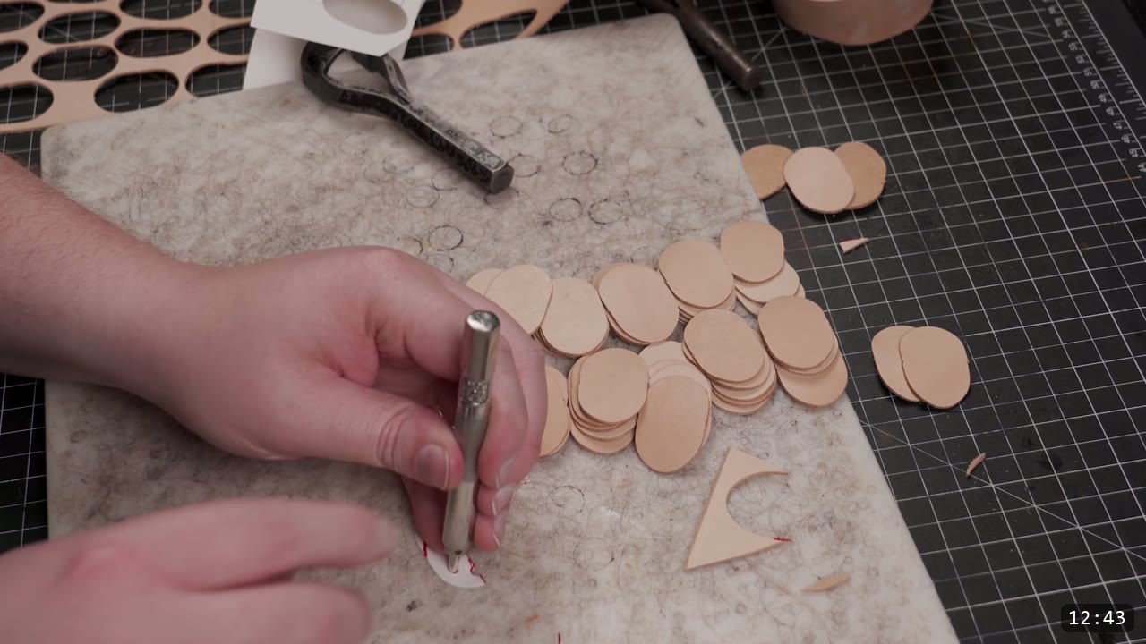 Articulating Leather Gauntlets Build Guide: A Fantasy Set from a Flat Pattern 10 a hand punching holes in small tan oval leather scale blanks on a felt pad, with piles of cut ovals alongside