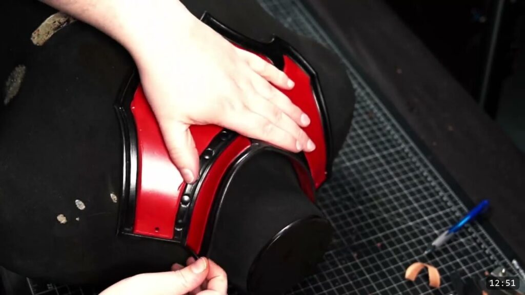 the assembled red and black gorget wrapped over a black dress form, hands pressing the collar into place to check the fit