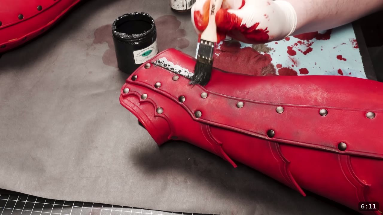 Leather Greaves Build Guide: From Flat Pattern to Antiqued Leg Armor 11 brushing a dark antique wash along the studded top edge of the red-dyed greave from a small jar, a second red greave in the background
