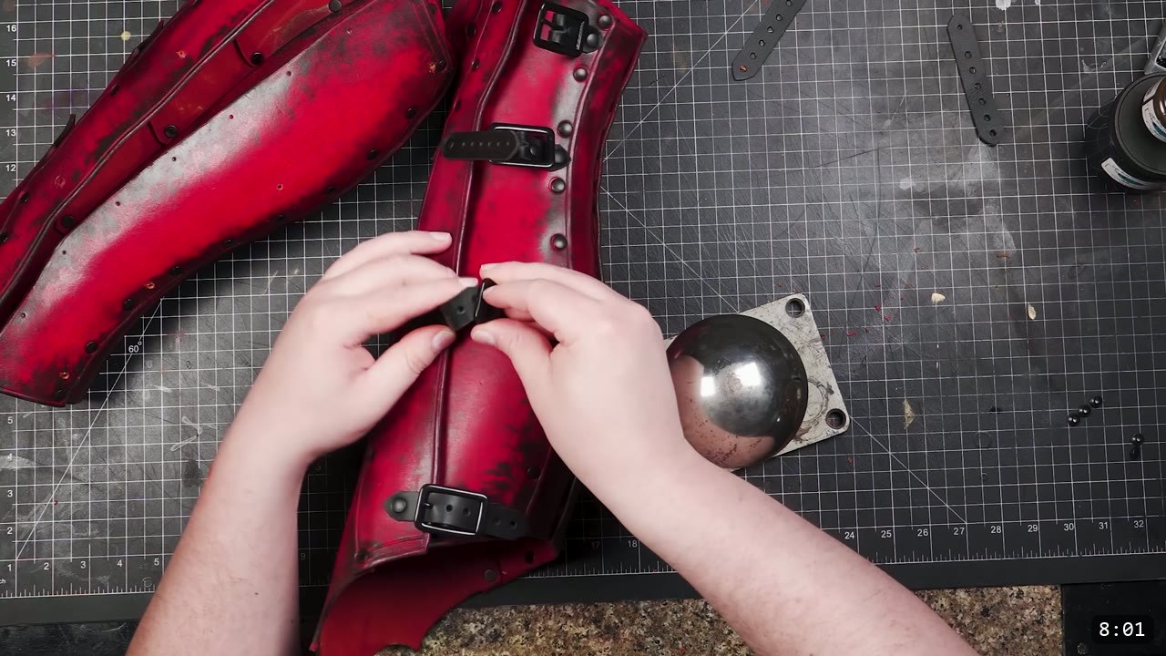 Leather Greaves Build Guide: From Flat Pattern to Antiqued Leg Armor 14 fitting a black buckle and strap to the finished pair of red antiqued greaves, a steel dome tool nearby
