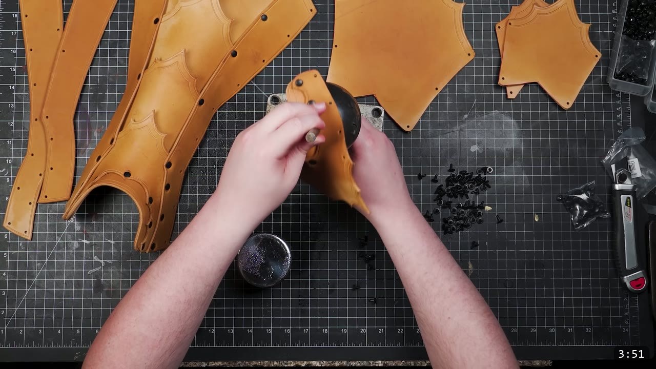 Leather Greaves Build Guide: From Flat Pattern to Antiqued Leg Armor 7 hands shaping a damp leather panel over a black dome form set on a metal plate, tooled greave panels laid out around it
