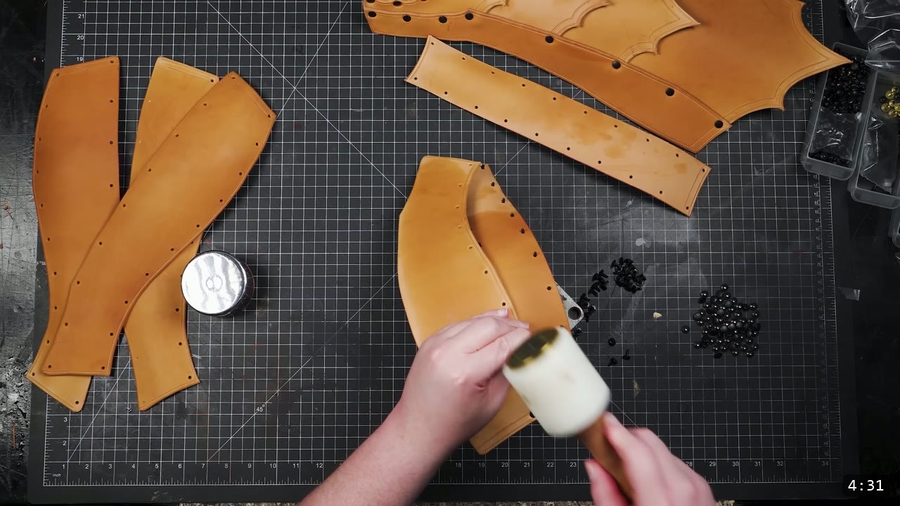 Leather Greaves Build Guide: From Flat Pattern to Antiqued Leg Armor 8 setting rivets on a greave panel with a white poly mallet against a round steel dome, black rivets scattered on the cutting mat