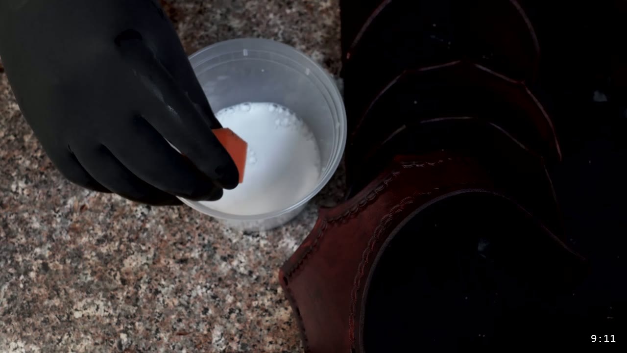 Leather Sabatons Build Guide: Foot Armor from a Flat Pattern 11 a gloved hand loading a sponge with milky acrylic finish beside stacked brown-stained sabaton plates on a granite slab