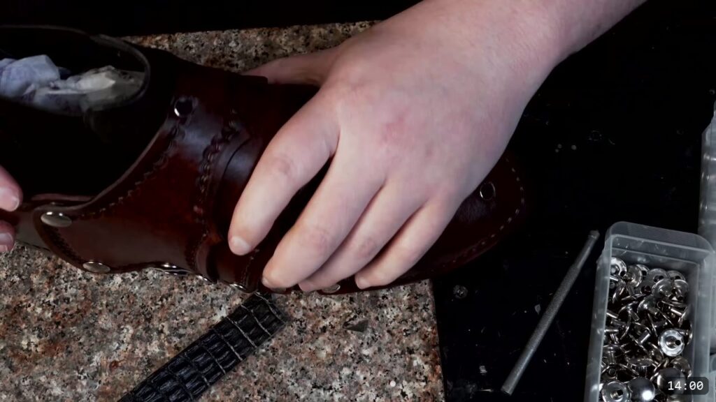 holding the finished brown sabaton, showing the suede-backed retainer strap, snaps, and tooled lames