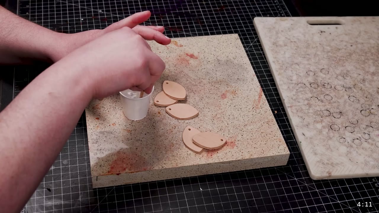 Leather Scale Armor Build Guide: A Flexible Scale Skirt from Scrap Leather 6 several cut tan scales and one holed scale laid out on a stone slab next to a small cup of finish being stirred
