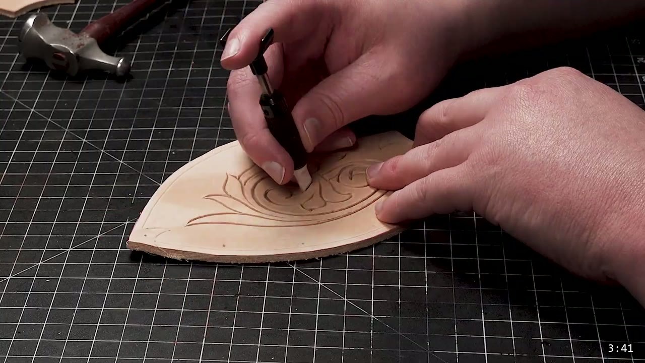 Fantasy Spaulders, Full Suit Version: Leather Shoulders That Mount to the Breastplate 4 a swivel knife carving a scroll design into a pointed tan vegetable-tan spaulder plate, a hammer resting on the mat behind it