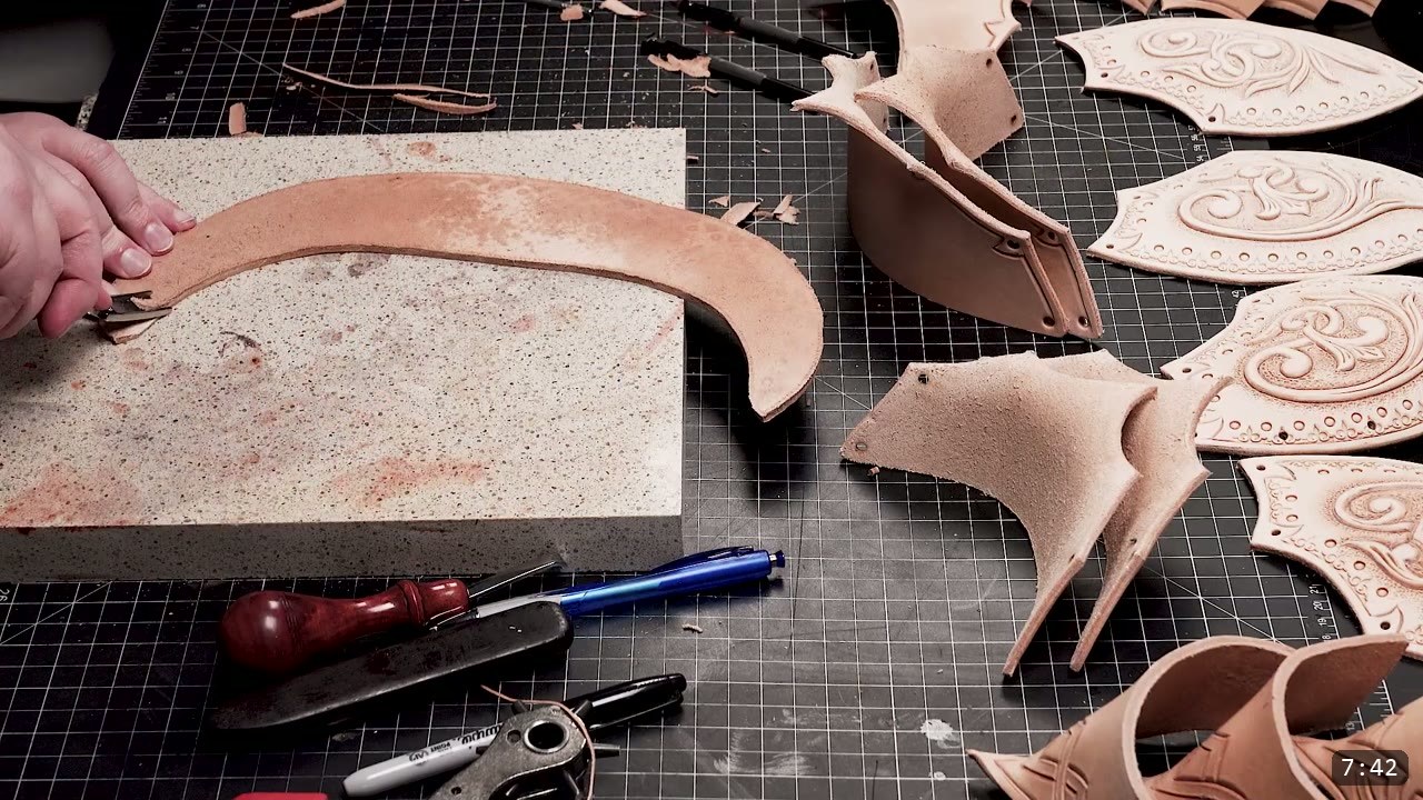 Fantasy Spaulders, Full Suit Version: Leather Shoulders That Mount to the Breastplate 7 a long tan leather strip resting on a granite slab beside several formed and tooled spaulder plates and flared trim pieces laid out on the bench, with an edge beveler and rotary punch nearby