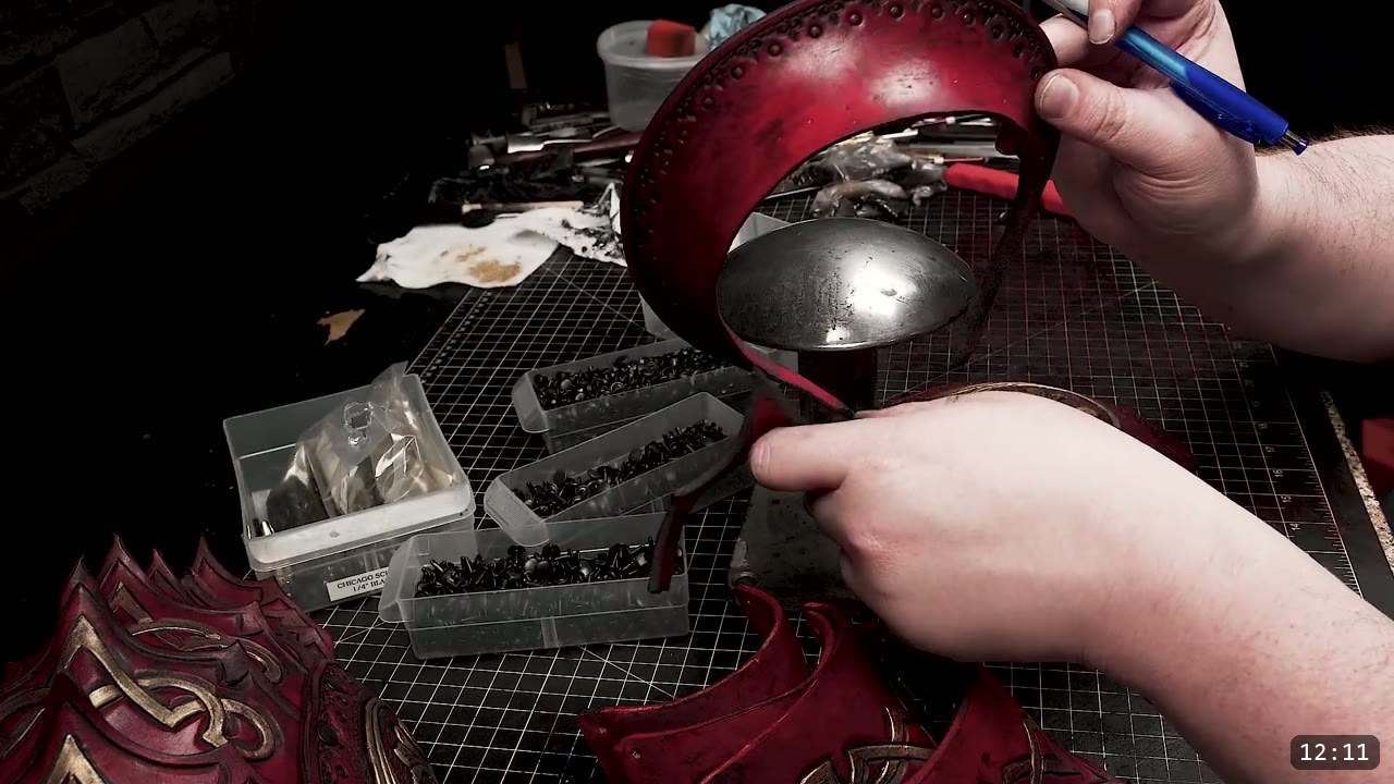 Fantasy Spaulders, Full Suit Version: Leather Shoulders That Mount to the Breastplate 10 a dyed deep-red domed spaulder crown held over a steel mushroom stake, with trays of black double-cap rivets and a box labeled Chicago Screws on the bench