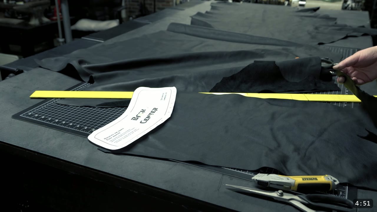Leather War Belt and Skirting Build Guide: A Fantasy Armor Waist from a Pattern 11 cutting a strip from a large black chrome-tan hide with a utility cutter, a Back Center pattern piece and scissors on the table