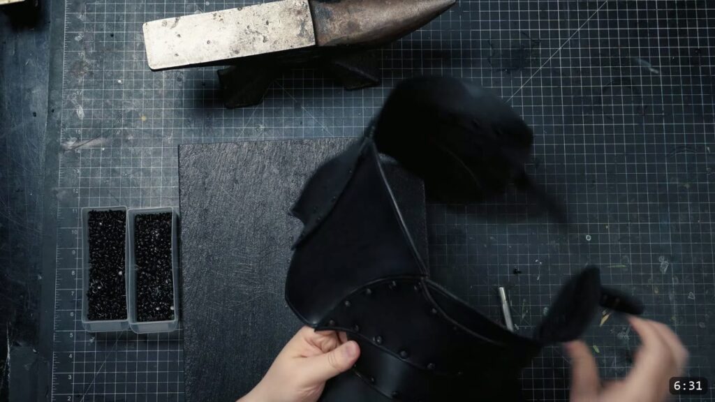riveting the chrome-tan skirt onto the assembled black war belt, a bin of black rivets and a granite slab on the bench