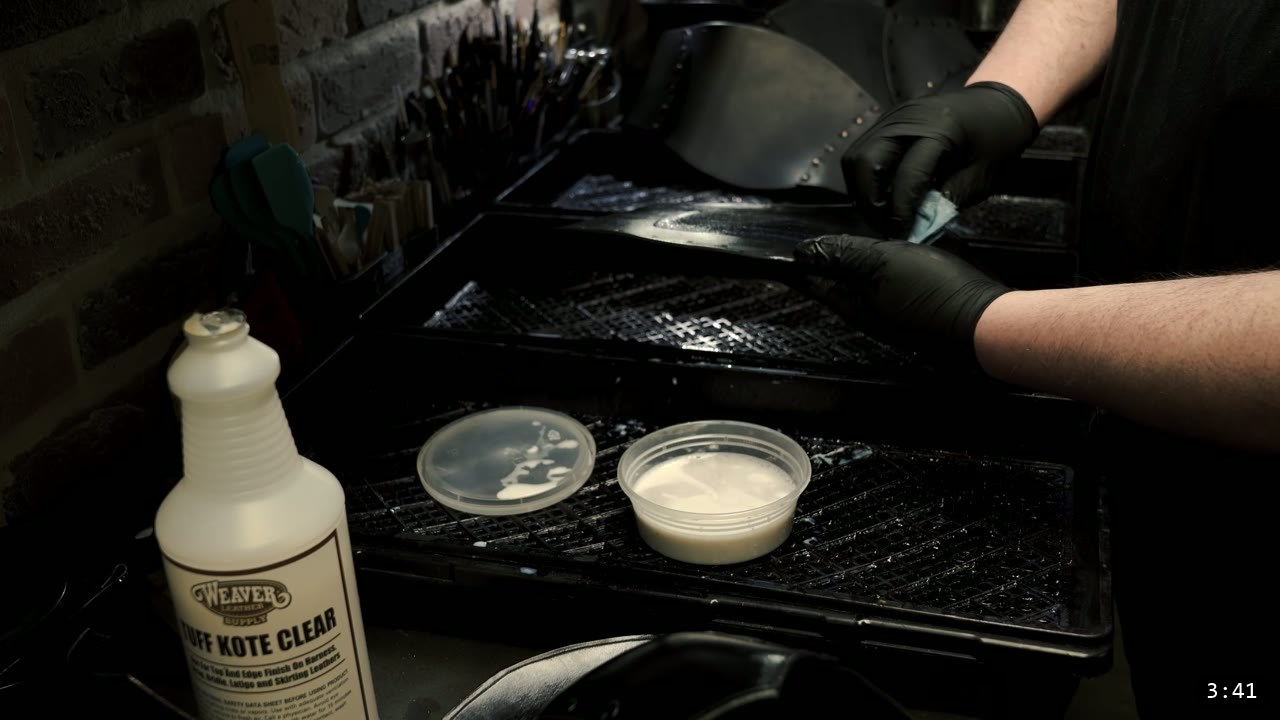 Leather War Belt and Skirting Build Guide: A Fantasy Armor Waist from a Pattern 9 a bottle of Weaver Tuff Kote clear finish beside gloved hands sealing the dyed-black belt pieces on a drying rack