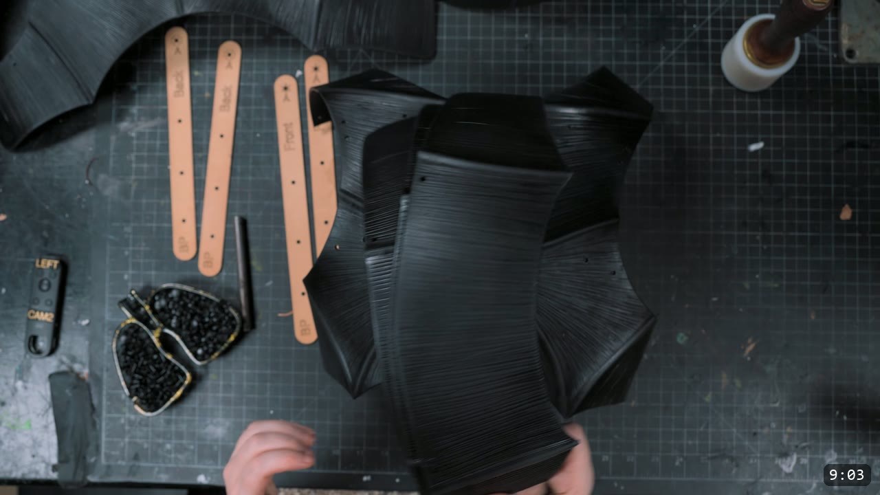 Finishing the Leather Berserk Armor: The Breastplate and Tassets Build Guide 11 dyed-black fluted breastplate pieces laid out with lettered tan retainer straps and a tray of black rivets, ready to assemble