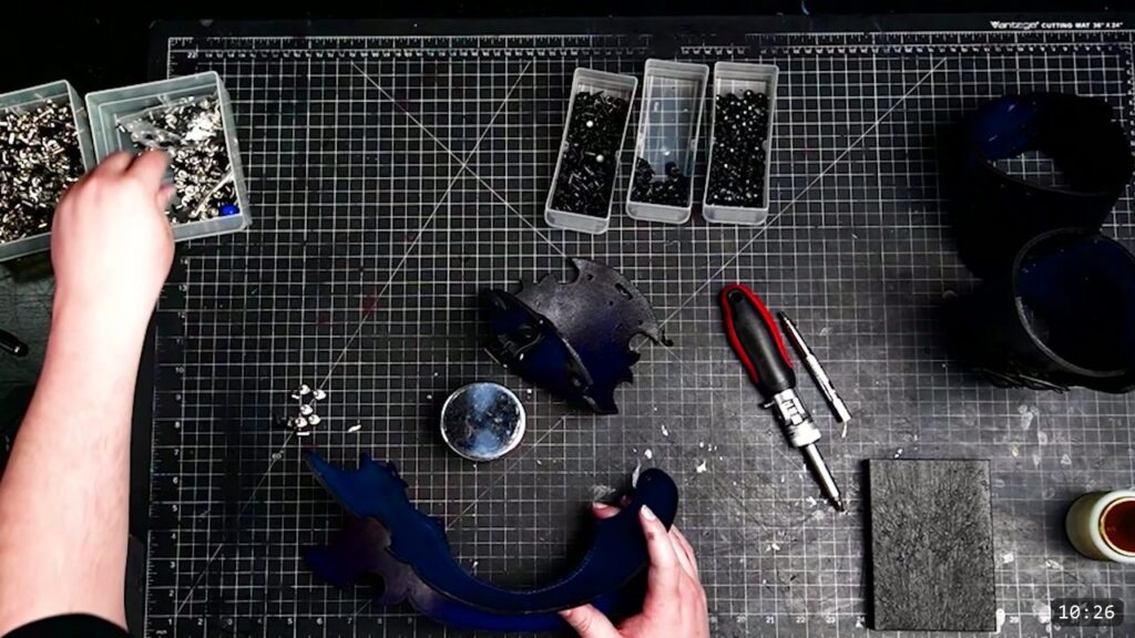 the domed elbow and curved lames laid out for final Chicago-screw assembly, with a screwdriver, a rivet setter, and a stone block on the bench