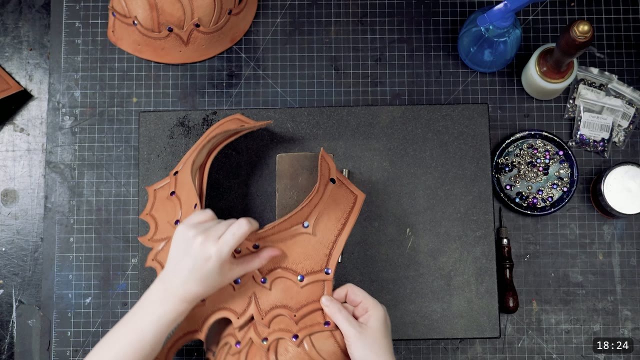 setting rivets on the tooled front torso panel with a wooden-handled awl and a dish of iridescent rivets on the bench