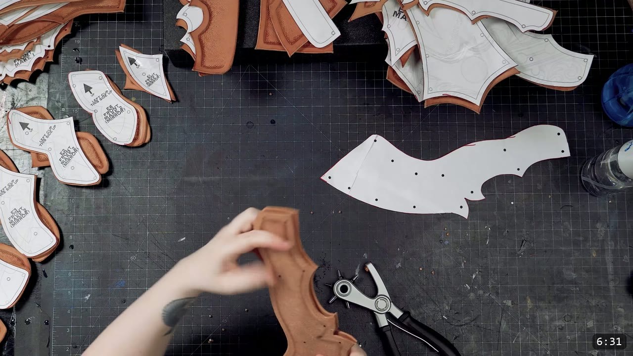 cut and tooled corset pieces with white paper patterns laid on top, hole positions marked, a rotary hand punch resting on the cutting mat