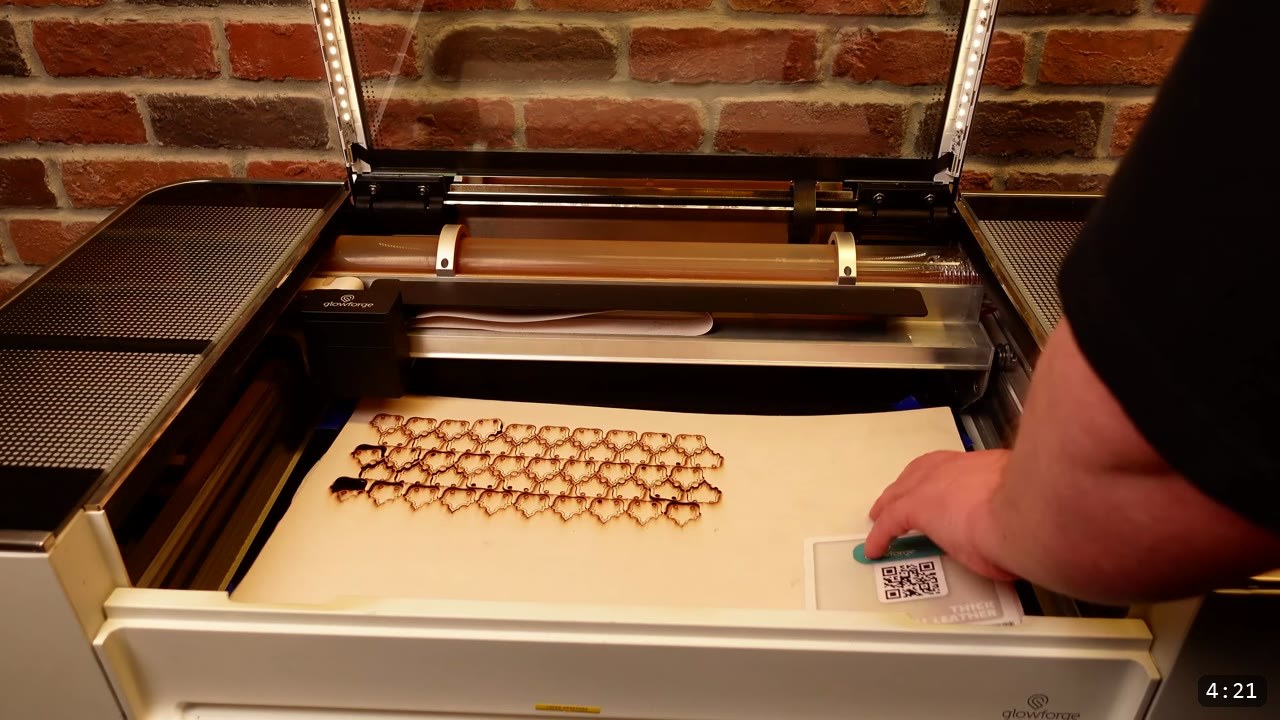 Articulating Leather Gauntlets Build Guide: Imperial Knight, Cut to Finish 3 a grid of small laser-cut leather finger scales in a Glowforge bed with a hand placing the QR-code settings card on the natural leather