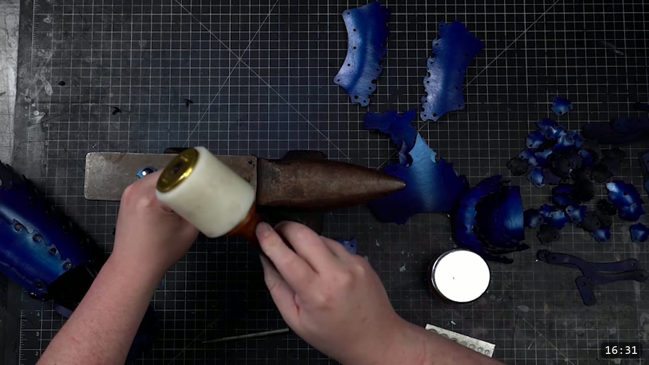 Articulating Leather Gauntlets Build Guide: Imperial Knight, Cut to Finish 7 a top-down view of a white poly mallet on a horned bench anvil, dyed-blue plates and a partly assembled blue cuff around it, and a tub of finish