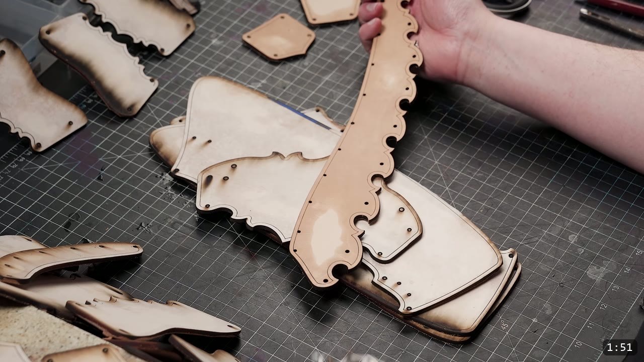 Leather Greaves Build Guide: Imperial Leg Armor from a Flat Pattern 2 cut vegetable-tan leather greave panels with scalloped edges laid out on a cutting mat, laser-burned edges visible