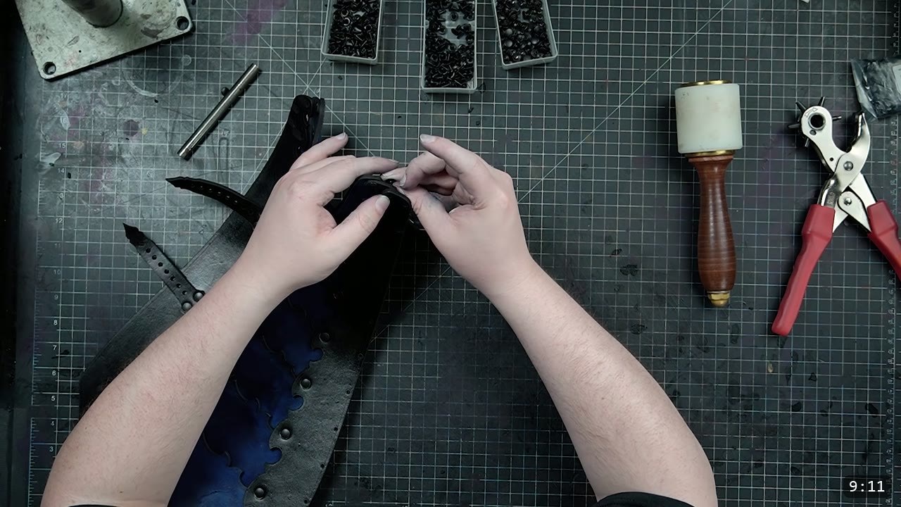 Leather Greaves Build Guide: Imperial Leg Armor from a Flat Pattern 11 hands snapping a black rivet into the assembled greave back section, a maul and rotary punch on the mat
