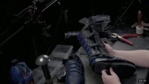 Roadmap Updates & Pre-Order Status 1 a finished black leather greave with blue lamellar scallops and side buckles, formed and fitted over a boot on the workbench