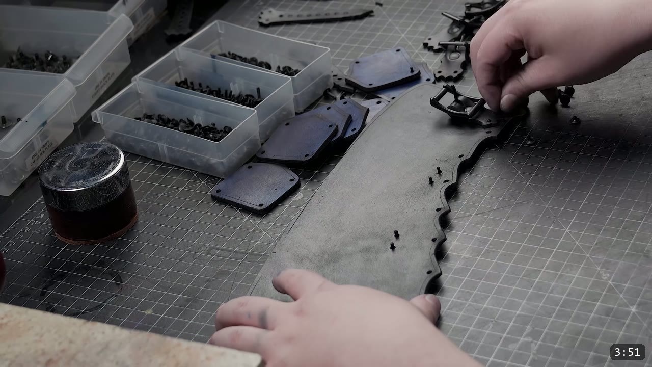 Leather Greaves Build Guide: Imperial Leg Armor from a Flat Pattern 5 dark-dyed leather panels with black double-cap rivets, buckles, and bins of hardware on a cutting mat