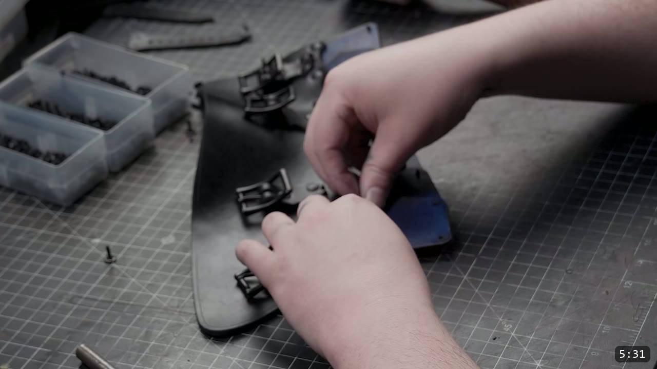 Leather Greaves Build Guide: Imperial Leg Armor from a Flat Pattern 7 fitting a black roller buckle to a dark leather greave side panel with rivet hardware nearby